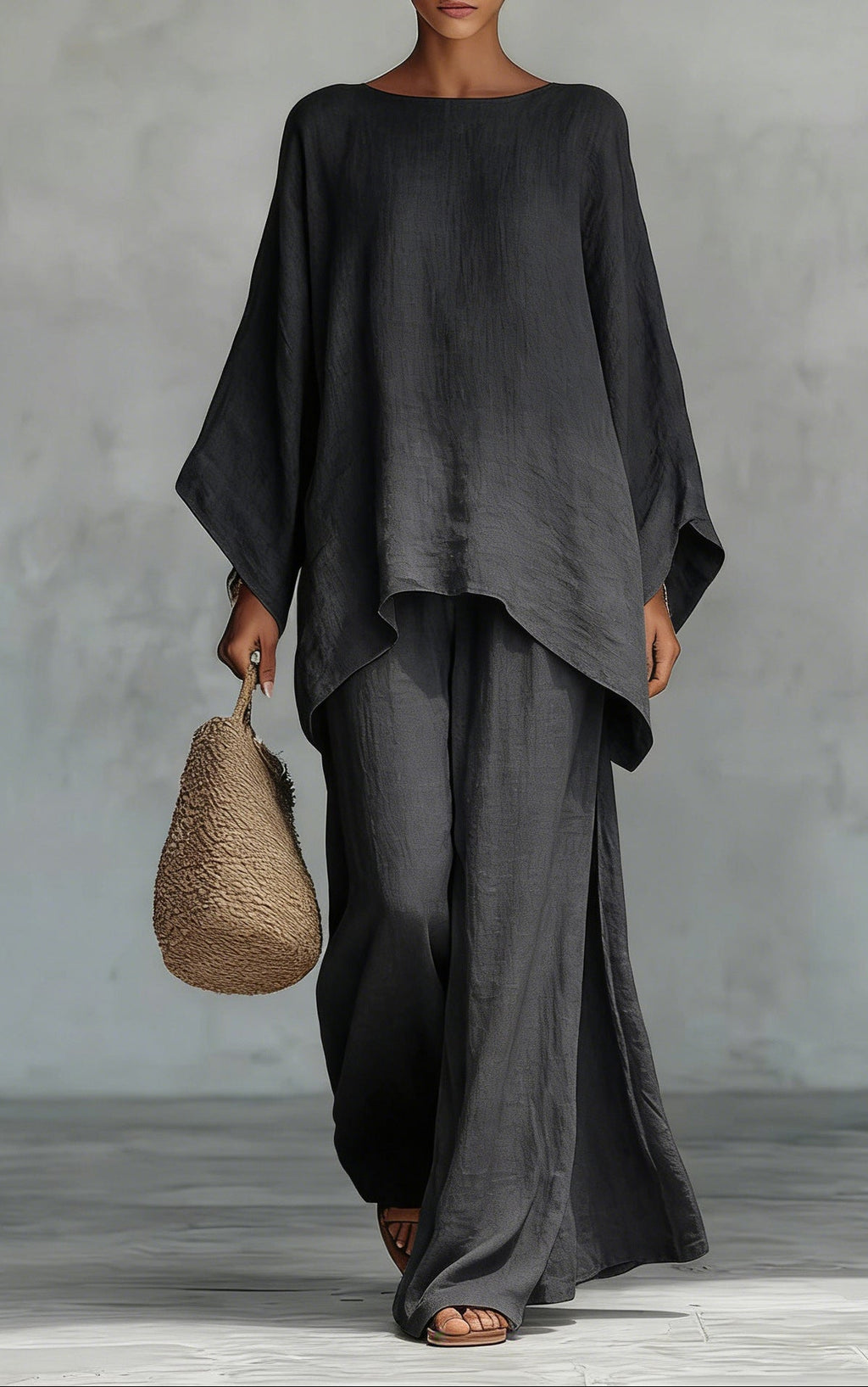 Person wearing a black outfit holding a woven bag against a gray background