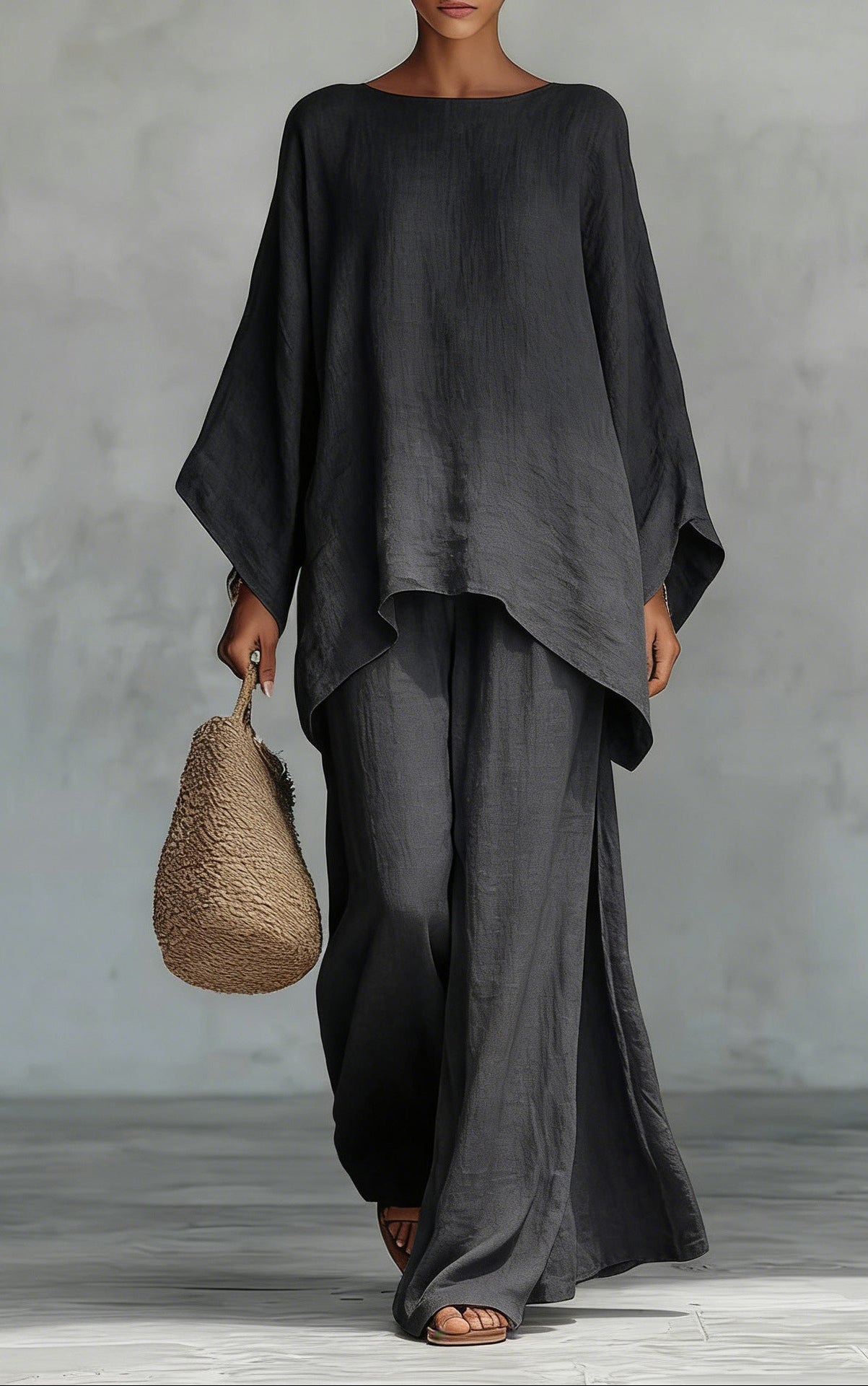 Person wearing a black outfit holding a woven bag against a gray background