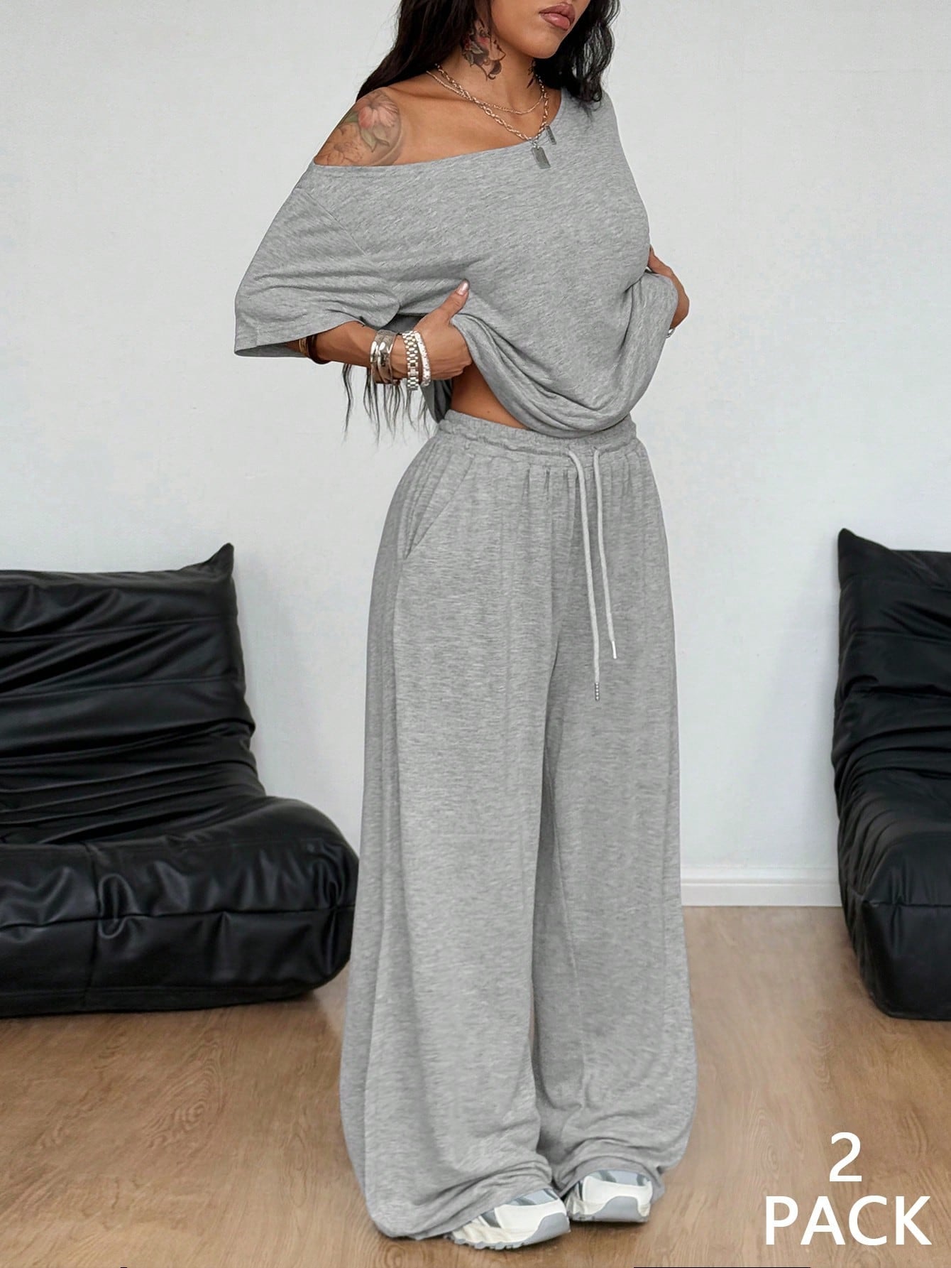 Woman wearing a gray off-shoulder top and wide-leg pants in a minimalistic room with black bean bags.