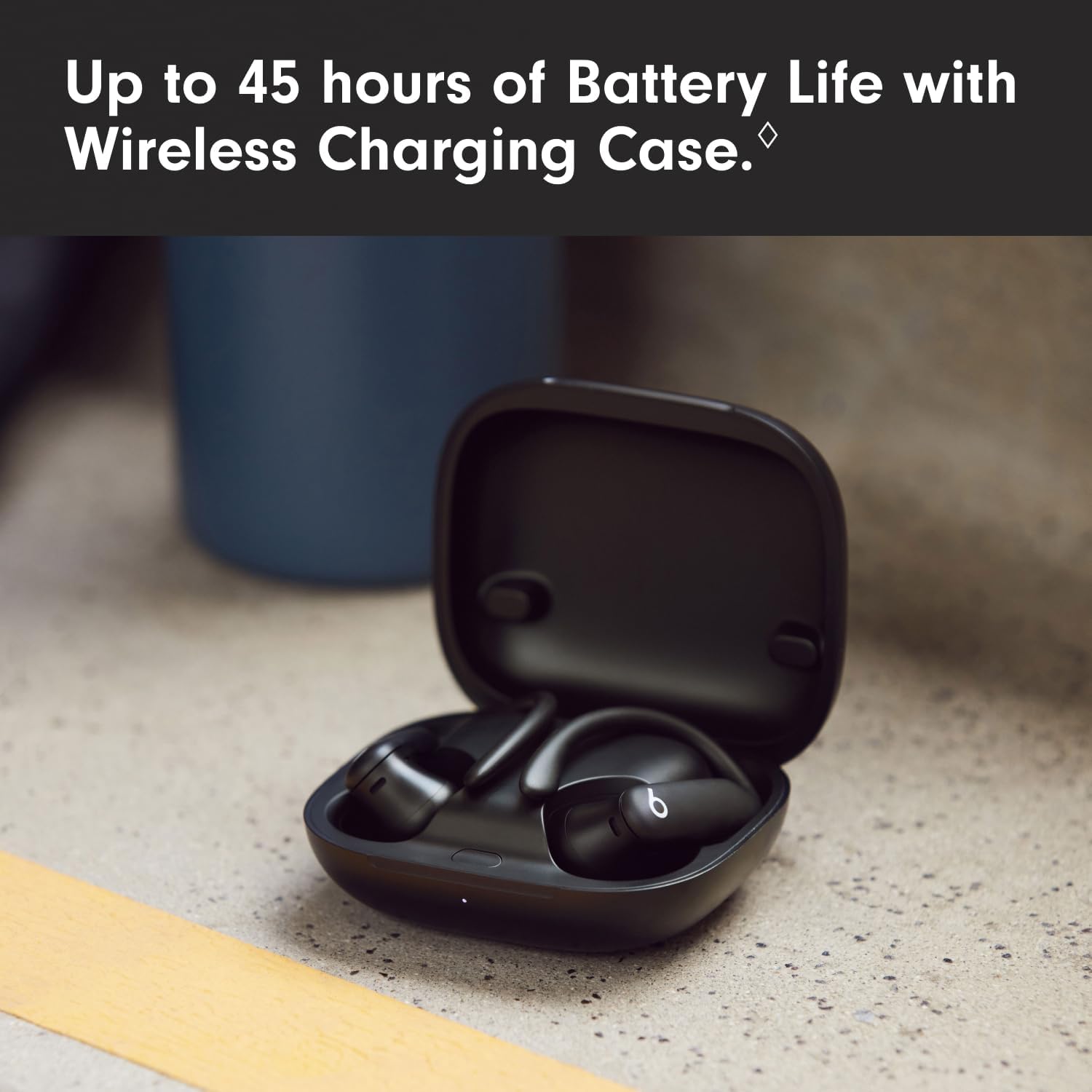 Black wireless earbuds in a charging case on a concrete surface with text about battery life.