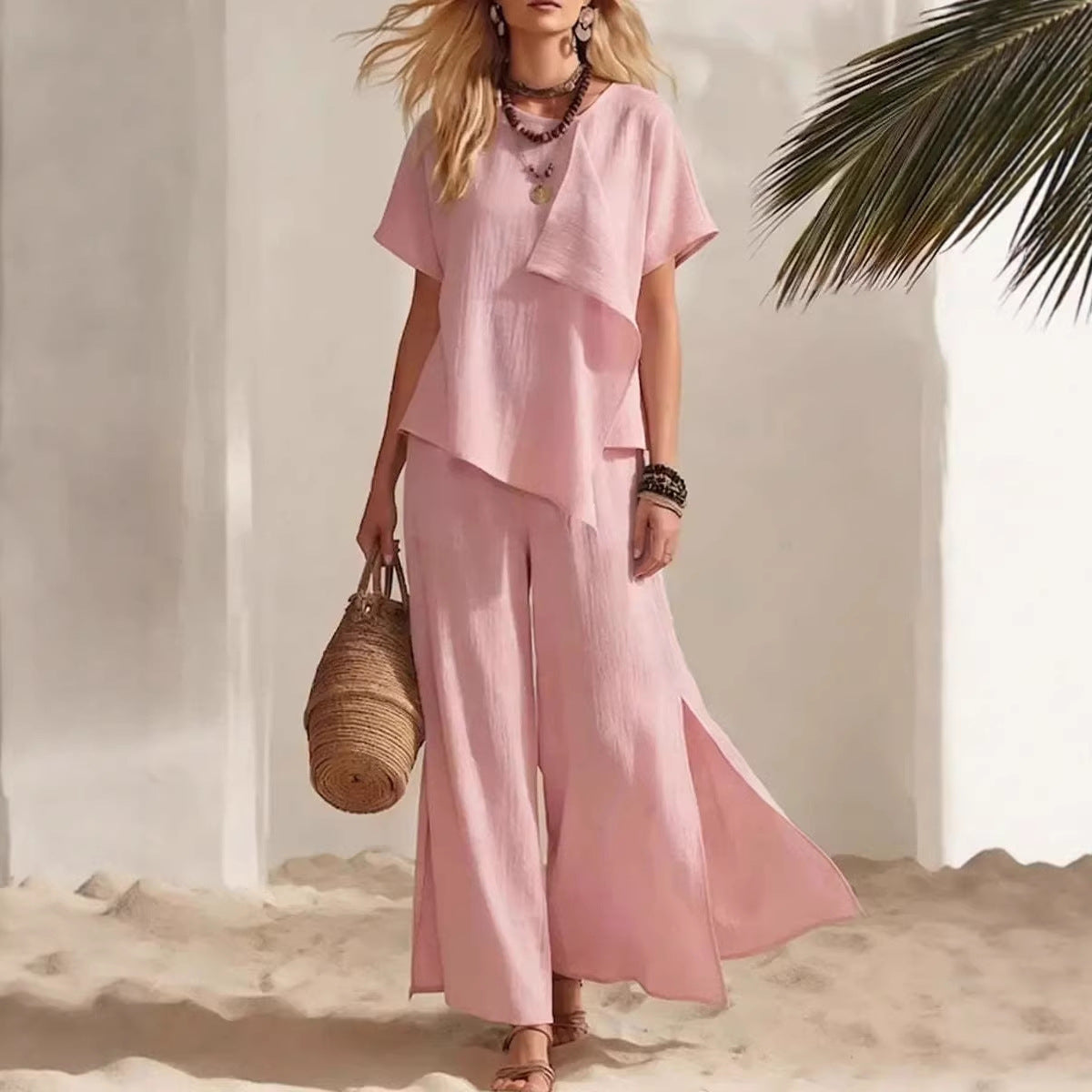 Woman in a pink outfit standing on sand with a palm leaf in the background