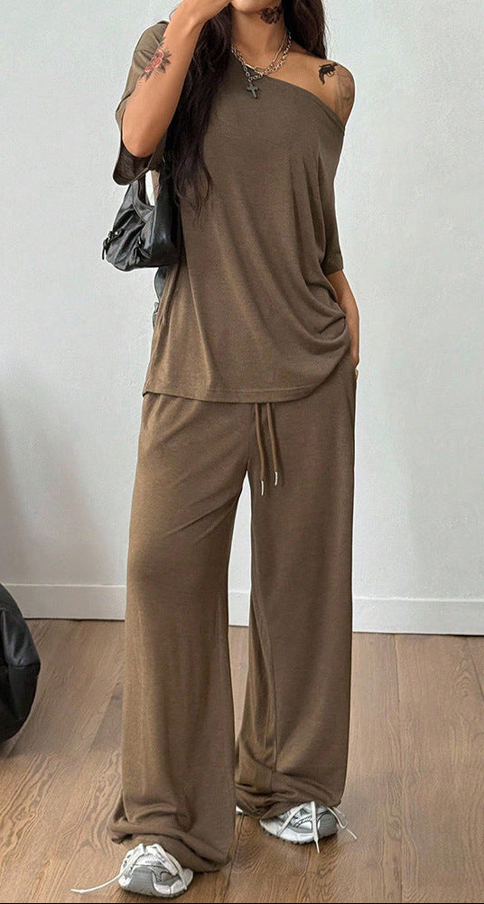 Person wearing a brown outfit with wide-leg pants and a matching top, standing against a plain wall.