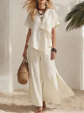 Woman in a white outfit holding a woven bag on a beach.