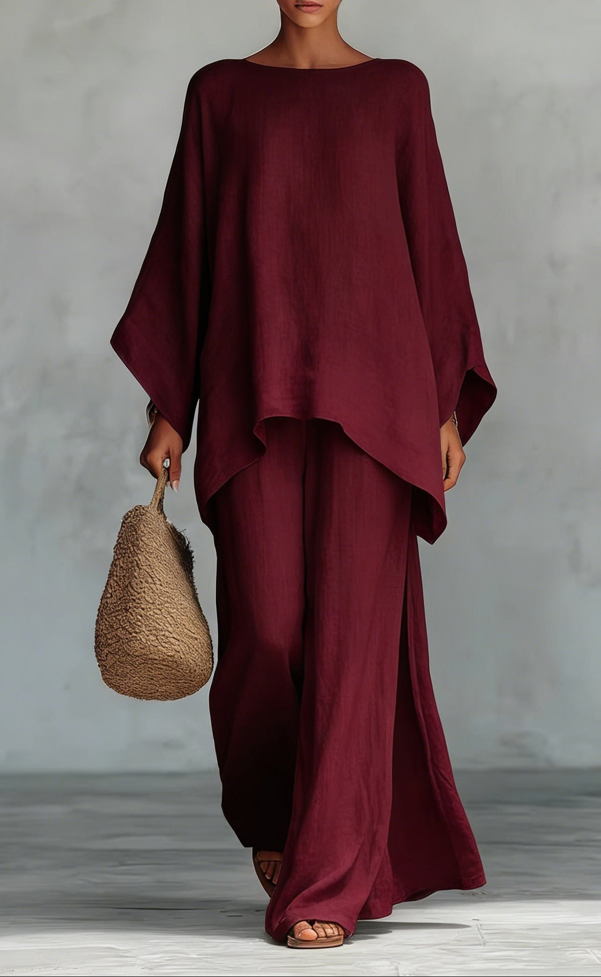 Person wearing a burgundy outfit holding a woven bag against a gray background