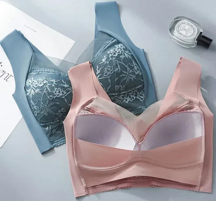 Two bras, one pink and one blue, on a light gray surface with a magazine and perfume bottle in the background.