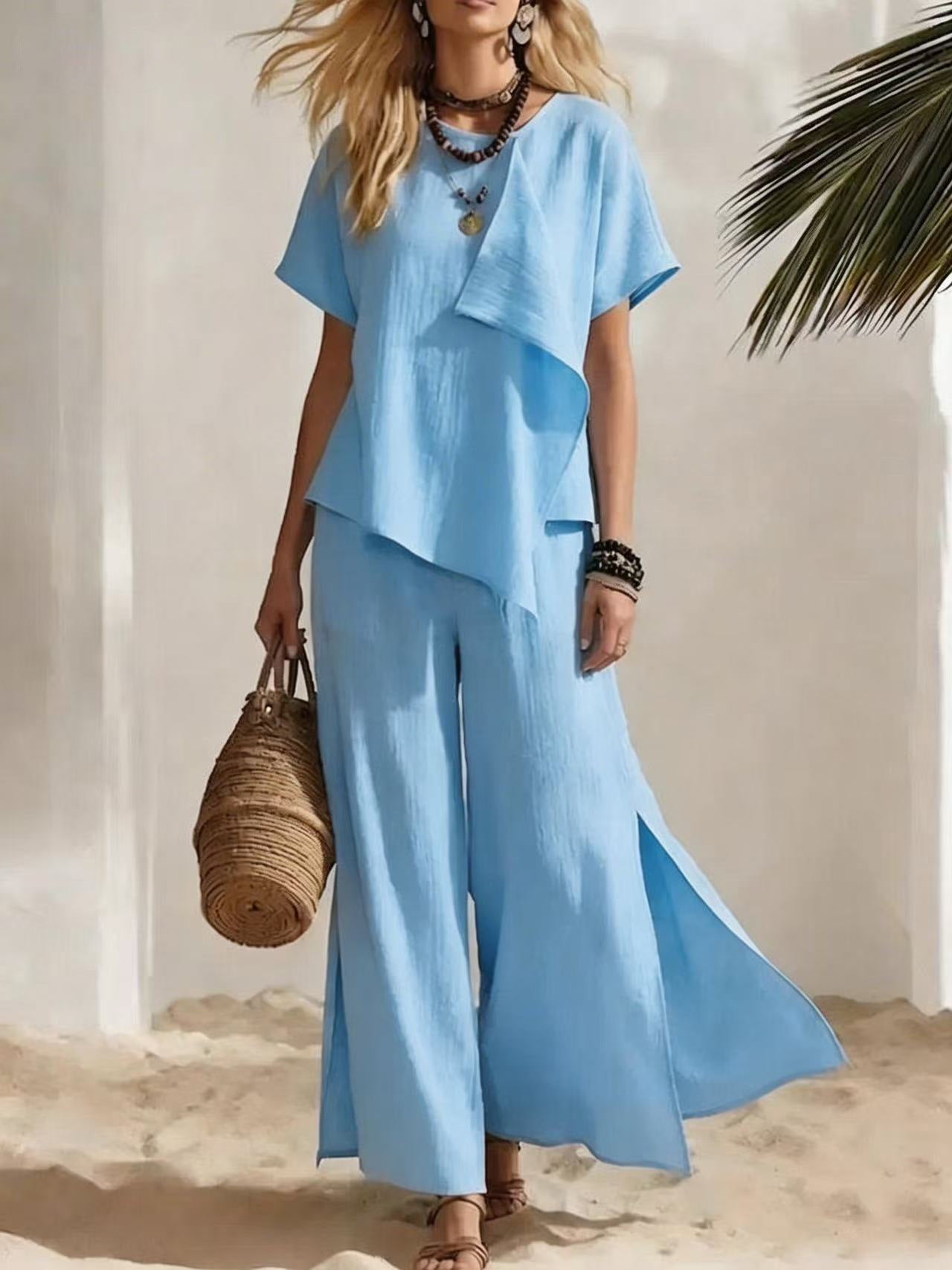 Woman in a light blue outfit holding a woven bag on a beach.