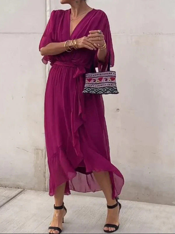 Woman wearing a vibrant pink dress holding a small handbag against a plain background