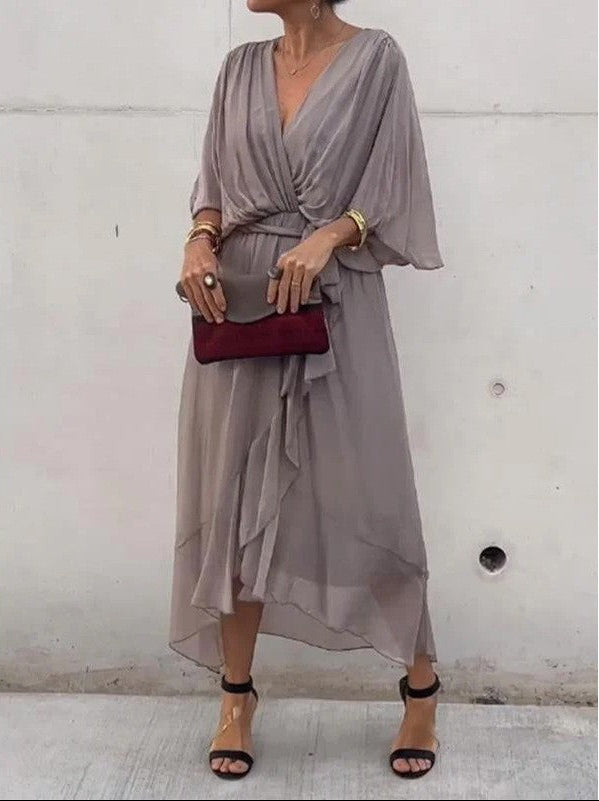 Woman wearing a gray dress holding a red clutch against a white wall.